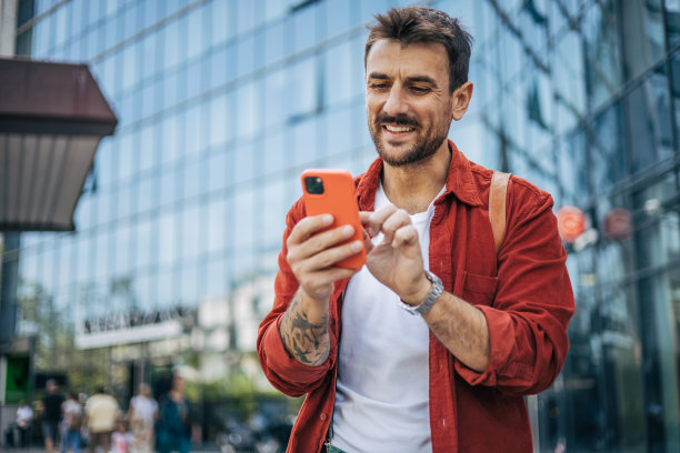 一个放松的男人走在街上，正在使用智能手机。图片下载