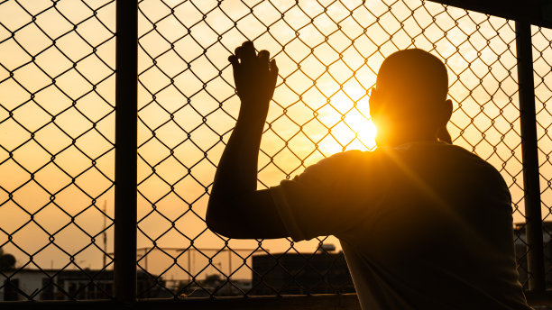 一个男人的剪影后面的栅栏，剪影照片的感觉心烦意乱，悲伤，不高兴或失望哭泣。青少年心理保健问题生活方式观念，失意无助地站着图片下载