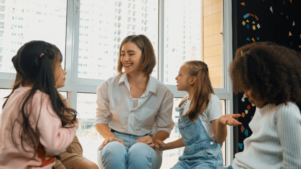 聪明的老师坐在地板上讲课，周围都是学生。博学。图片下载