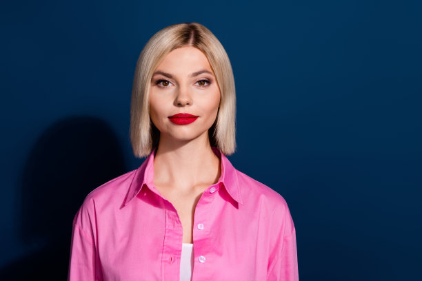 可爱的严肃的女人的照片，鲍勃发型，红色的伴侣口红，穿着粉红色的衬衫，看着你孤立的深蓝色背景图片下载