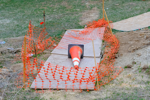 橙色施工围栏和交通锥铺设在路边的棕色纸板泥土路基上。基础设施维修施工现场维护工作人行道路边城市街景照片图片下载