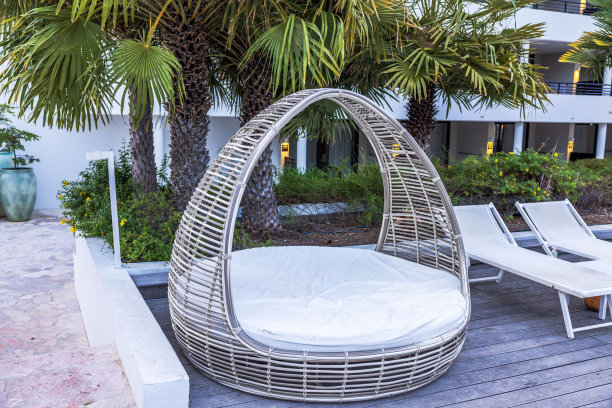 一个舒适的篮式柳条躺椅的特写视图依偎在棕榈树附近的室外酒店游泳池。库拉索岛。图片下载