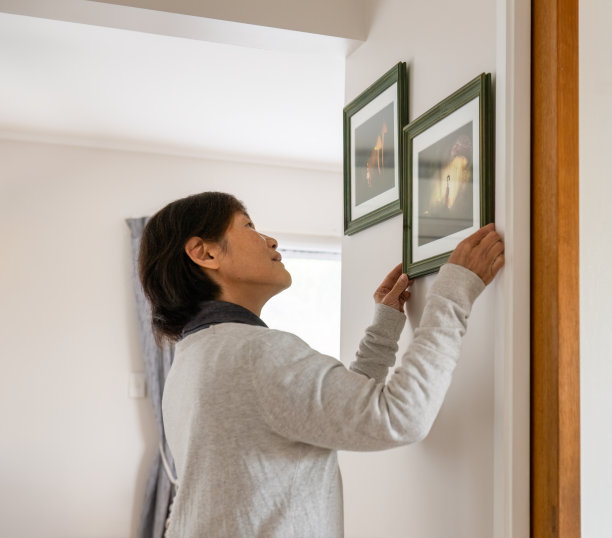 在家里墙上挂画的女人。相框里童话般的发光蘑菇照片。图片下载