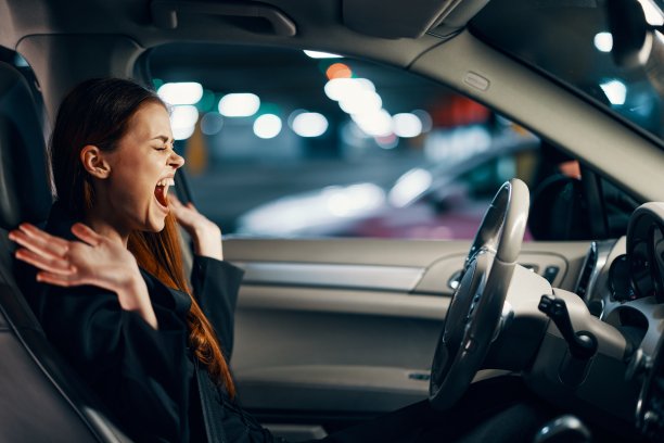一名女子穿着黑色衬衫，系着安全带，坐在汽车方向盘后面，双臂张开，表达着自己的情绪。从侧面拍摄的关于道路安全主题的照片图片下载