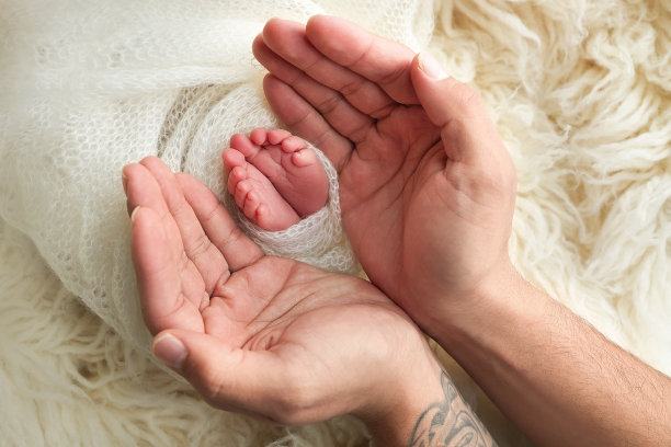 爸爸的手心，妈妈的脚上都抱着刚出生的婴儿的白毯子。新生儿的脚放在父母的手掌上。工作室微距照片的一个孩子的脚趾，脚跟和脚图片下载
