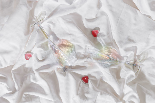 浪漫的概念，生活方式照片的简约风格，两个明亮的眼镜与彩虹阴影，粉红色蜡烛心形在床上与白色床单在家里，自然光，俯视图近距离，copyspace图片下载