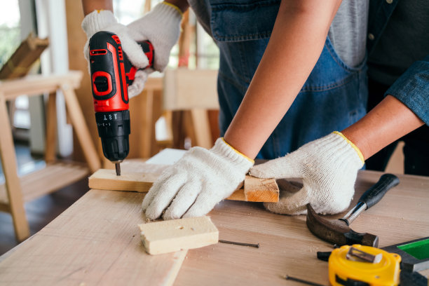 亚洲父亲和儿子的工作是木工或木匠。近距离的父亲和他的儿子的手钻洞在一块木板小心翼翼地在一起。在家庭工作室做木工。图片下载