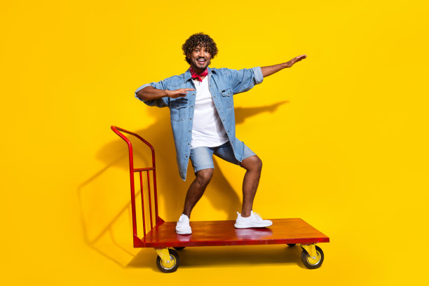 漂亮的年轻男性的全尺寸照片骑冲浪仓库推车穿时髦的牛仔服装红色围巾孤立的黄色背景图片下载