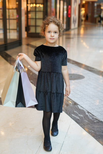 可爱的小女孩穿着黑色的衣服在购物，小孩拿着购物袋。黑色星期五概念图片下载