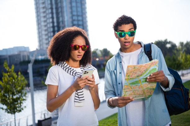 年轻的两个惊讶的朋友游客戴着太阳镜拿着导航纸地图和电话探索新的城市户外的照片图片下载