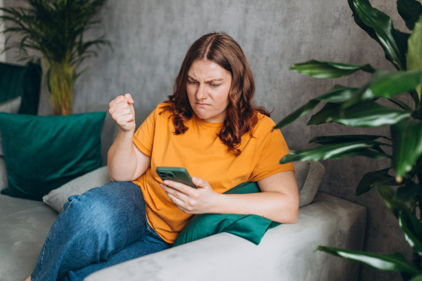 心烦意乱的年轻女子用手机看坏消息，伤心的女孩坐在家里沉思。消极的人的情绪。红发女人拿着智能手机，看着屏幕图片下载