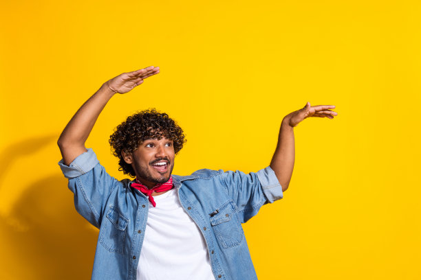 照片中英俊的年轻人举手跳舞，空着空间，穿着时髦的牛仔服装，红色的围巾孤立在黄色的背景上图片下载