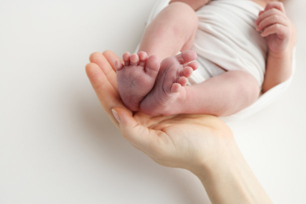 爸爸的手心，妈妈的脚上都抱着刚出生的婴儿的白毯子。新生儿的脚放在父母的手掌上。工作室微距照片的一个孩子的脚趾，脚跟和脚图片下载