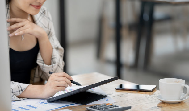 美女坐在家里办公室用笔用数码平板电脑的剪裁照片。图片下载