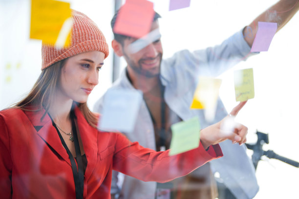 业务团队在会议期间使用贴满便签的玻璃墙来概述流程。敬业的同事们聚集在一个玻璃头脑风暴板周围。构思想法和策略。图片下载