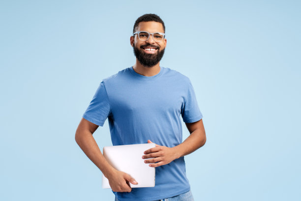 快乐的非裔美国人，戴着眼镜，拿着笔记本电脑，看着蓝色背景的相机图片下载