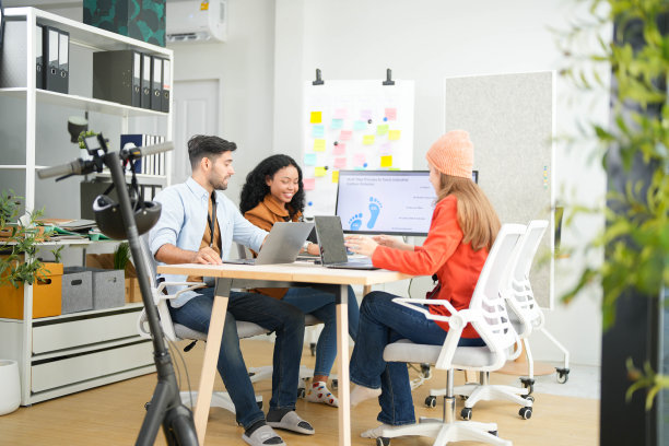 创意团队在一个现代化的办公室里用笔记本电脑和数字屏幕合作一个项目，用相机记录。年轻的商业分析师在生态战略的屏幕上评估环境绩效。图片下载