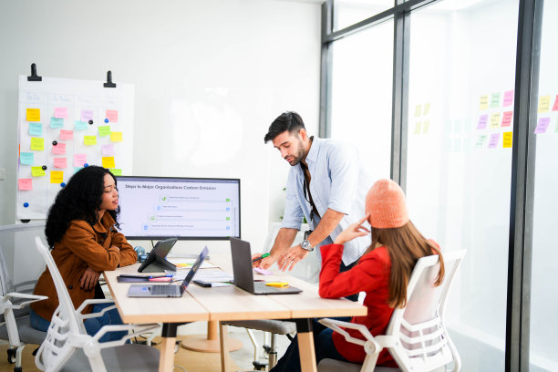 创意团队在一个现代化的办公室里用笔记本电脑和数字屏幕合作一个项目，用相机记录。年轻的商业分析师在生态战略的屏幕上评估环境绩效。图片下载