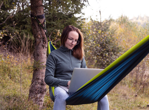 一个女人在山上的吊床上用笔记本电脑工作图片下载