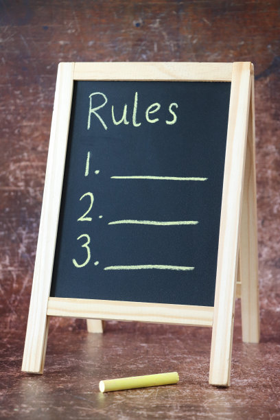 木制a框板黑板的特写图像，表面是黄色的粉笔棒，粉笔上写着“规则”的标题和编号的项目列表，书写的水平线，棕色背景图片下载