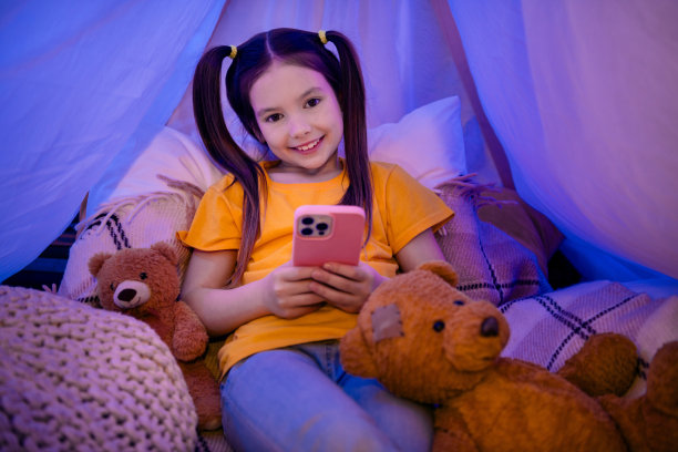 照片中可爱的小女孩躺在地上，晚上抱着小玩意，穿着时髦的黄色服装的幼儿园小朋友的室内图片下载