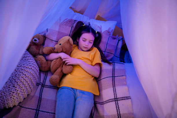 照片里可爱的小女孩躺在地板上睡觉，晚上抱着玩具穿着时髦的黄色服装的幼儿园小朋友图片下载