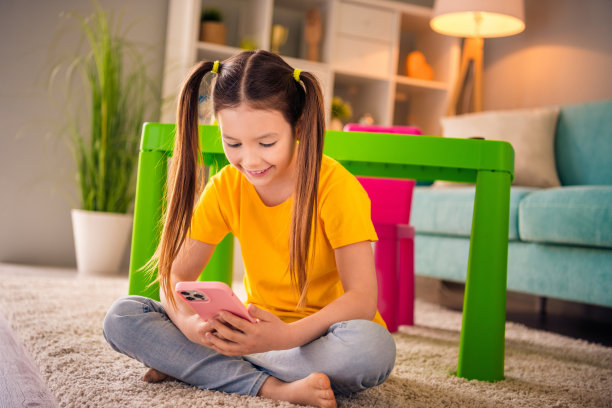可爱小女孩的照片肖像坐在地板上拿着设备连接wifi穿着时髦的黄色服装学龄前儿童幼儿园内部图片下载