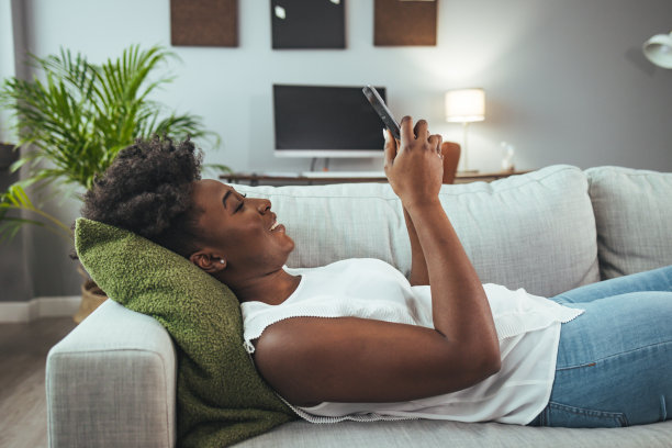 一个年轻女子在家里沙发上休息时玩手机的照片图片下载