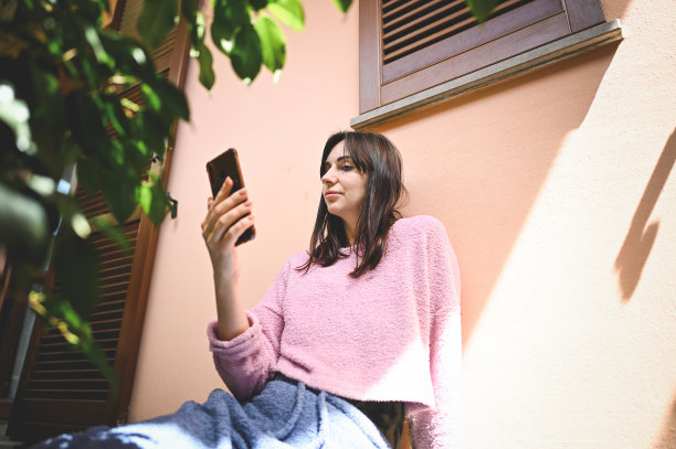 千禧一代女性在阳光明媚的露台上看智能手机的照片。图片下载