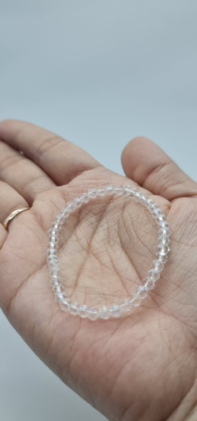 手里拿着一只手工制作的白色水晶手镯，黑底盒子，孤立在白底中。图片下载