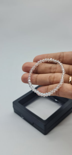 手里拿着一只手工制作的白色水晶手镯，黑底盒子，孤立在白底中。图片下载