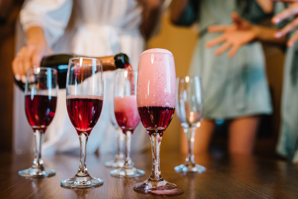 女孩们在睡衣派对上往杯子里倒香槟。欢快的伴娘庆祝单身派对的特写照片。女性吃吐司配酒。性感女孩最好的朋友穿浴袍。图片下载