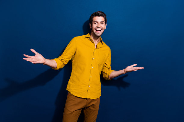漂亮的年轻男性的照片肖像，举手说话，穿着时髦的黄色衣服，在深蓝色的背景上孤立图片下载
