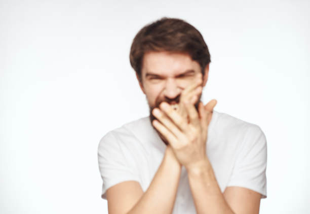 一个留着胡子的情绪化的男人在一张浅色背景裁剪的照片中把手放在脸附近图片下载