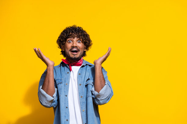 漂亮的年轻男性的照片肖像举起双手震惊的脸穿着时尚的牛仔服装红色围巾孤立在黄色背景图片下载