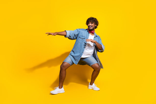 英俊的年轻人跳舞的全身照片好心情穿着时髦的牛仔服装红色围巾孤立的黄色背景图片下载