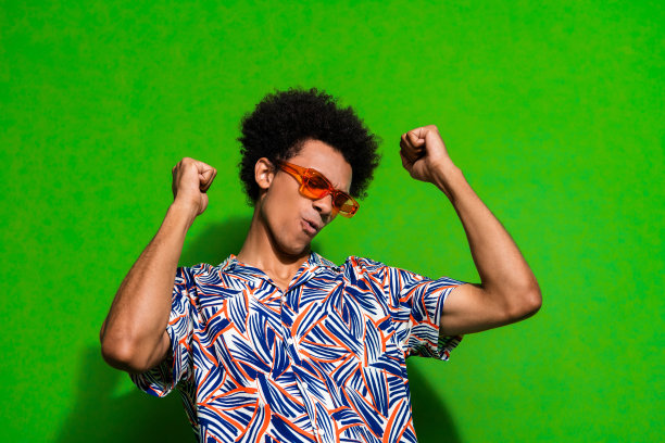 照片开朗积极的男人穿着印花衬衫深色眼镜有乐趣上升的拳头是空的空间孤立的绿色背景图片下载