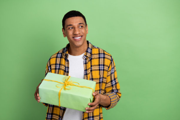 照片中开朗开朗的男人露出牙齿微笑，拿着礼盒，在绿色的背景上看起来空无一物图片下载