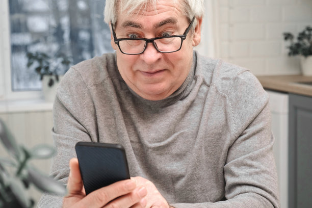 白发苍苍的老人看着网络摄像头，拿着手机，和孩子聊天，老婆上网。老爷爷微笑着与朋友、家人视频聊天。现代科技和老一辈。图片下载