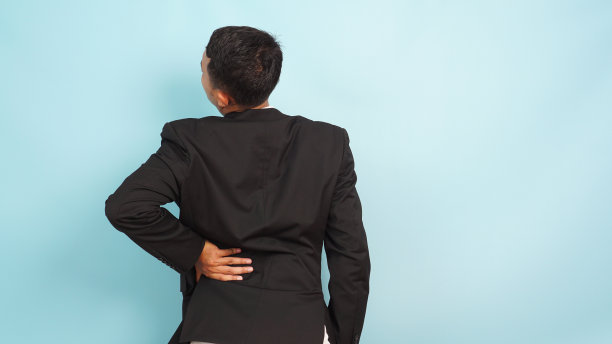 腰酸背痛的年轻亚洲商人，腰捂着腰，站在蓝色背景上图片下载