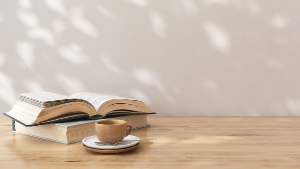 褐色的木质台面，打开的书和咖啡杯在斑驳的阳光下，背景是白色墙壁上的叶影图片下载
