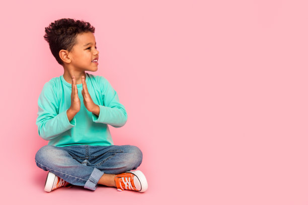 可爱小男孩的全身照片坐在地板上拍手，看起来空无一物，穿着时髦的海蓝宝石服装，孤立在粉红色的背景上图片下载