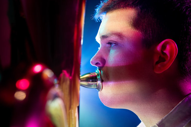 有才华的人，艺术音乐家坐着，在柔和的蓝粉色舞台灯光下演奏小号的近景照片。图片下载