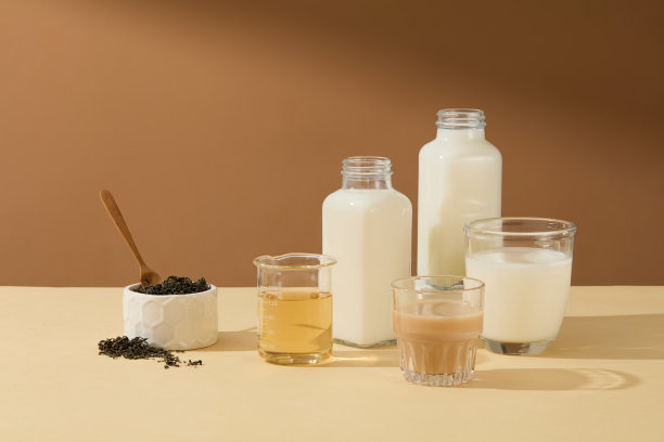 早餐喝几杯饮料，一杯茶，一瓶暖棕色背景的鲜牛奶或牛奶咖啡，一些干茶叶放在白色的圆碗里，用木勺。广告照片正面视图图片下载