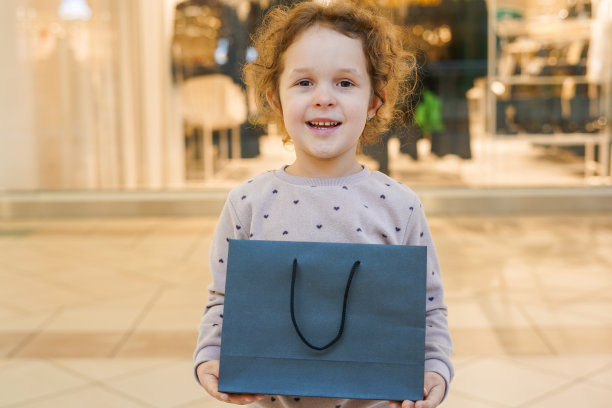 可爱的小女孩，卷发，在布店拿着黑色的购物袋图片下载