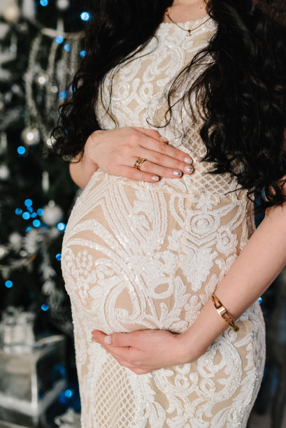 孕妇在家里的圣诞树旁摆姿势。圣诞快乐，节日快乐。怀孕，人与期望的概念。女人抱着肚子。婴儿洗澡。关闭了。图片下载