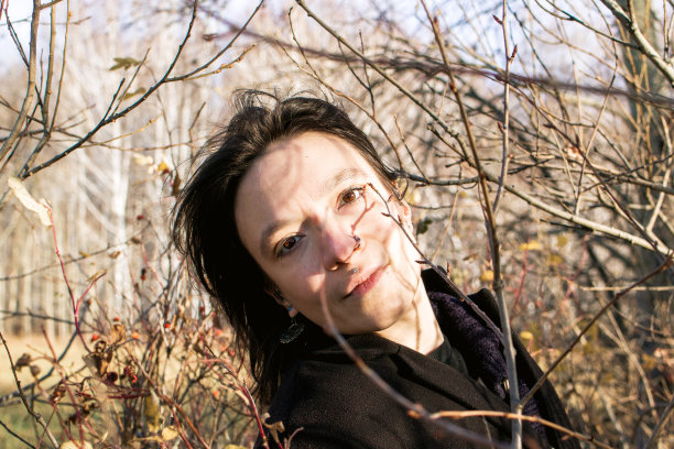 穿着黑色外套的长发年轻女子站在灌木丛中沉思图片下载