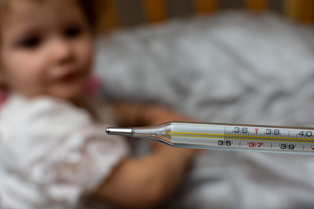 一个蹒跚学步的孩子躺在床上，旁边有一个医用体温计图片下载