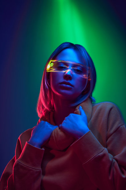 融合了轻松的街头风格和科技灵感的配件。在霓虹灯下，年轻女孩在渐变的绿蓝色背景下摆姿势图片下载