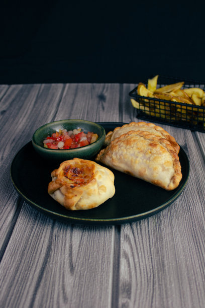 两个肉馅卷饼和一个篮子放在一个深色的盘子里，阿根廷菜，青玉辣酱和青玉辣酱图片下载